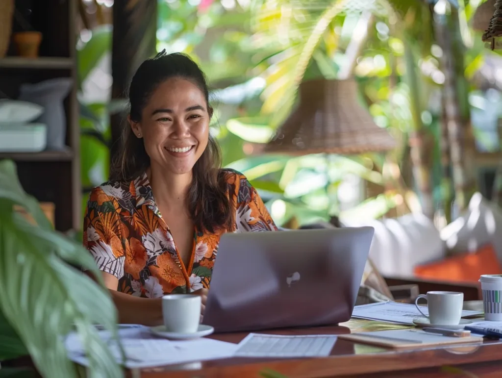 Smiling entrepreneur in Bali working on laptop at tropical café, reviewing business reports and enjoying morning coffee